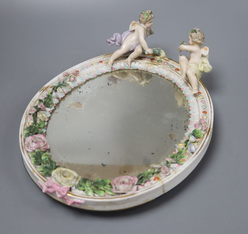 A German floral encrusted porcelain wall mirror, surmounted with winged cherubs, overall length 33cm